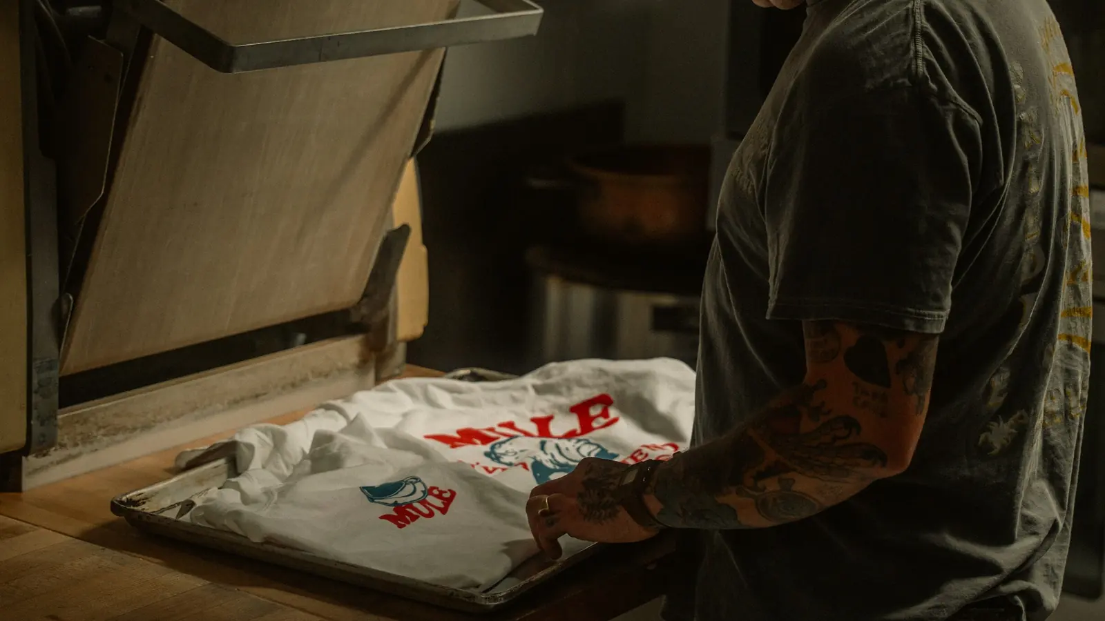 Persona preparando una camiseta personalizada junto a una prensa térmica