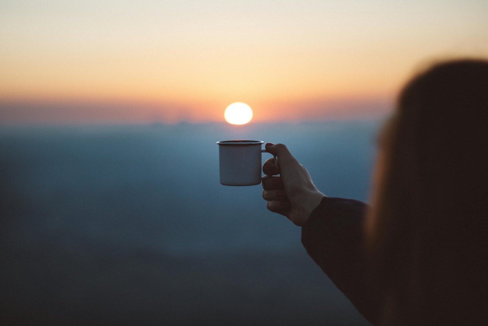Capacidad de Adaptación 2025: Clave para una Vida Plena y Motivada. 4 Mujer sujetando una taza en una pueta de sol. La capacidad de adaptación favorece nuestro bienestar