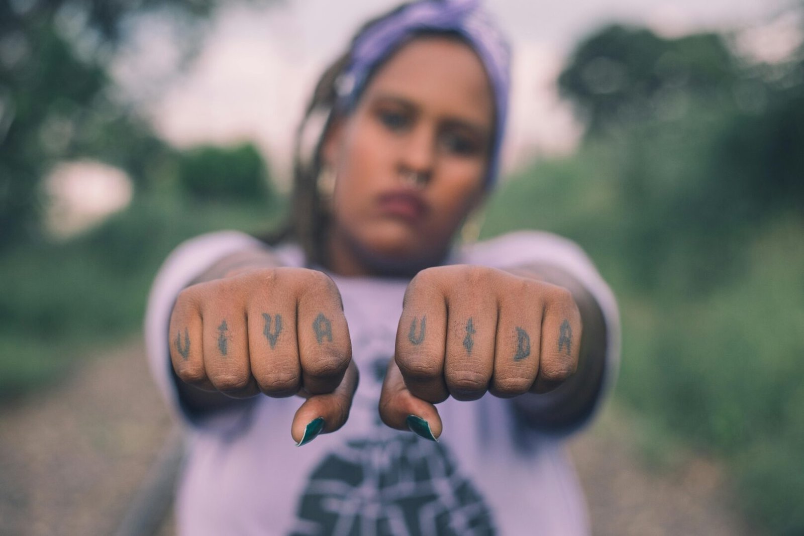 Close-up of a woman showcasing 'Viva Vida' tattoos on her fists in an outdoor setting.